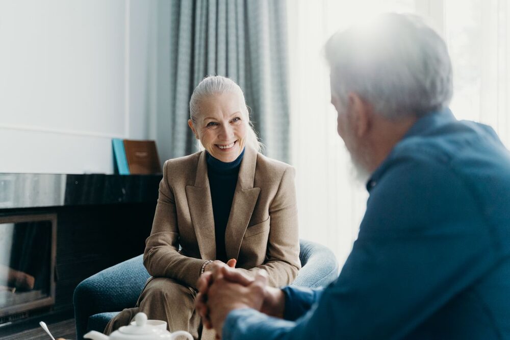 A senior couple sitting together warmly at home, having a quiet conversation.