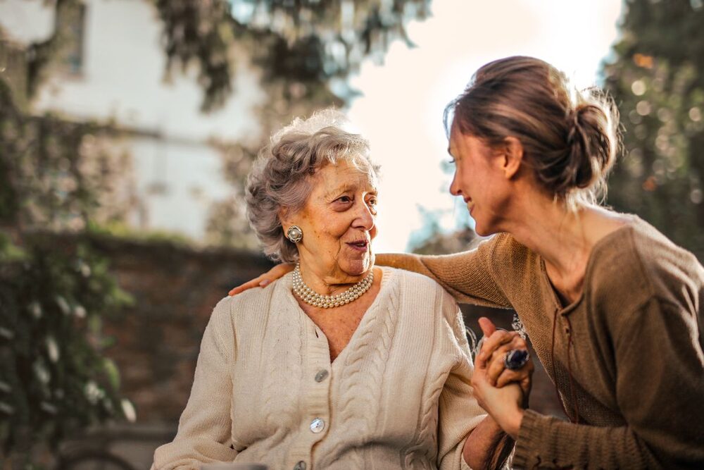 An adult daughter embracing her elderly mother warmly outdoors.